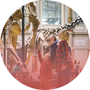 Two adults and a child standing in the dinosaur hall of the Museum of Natural History, surrounded by large fossil skeletons